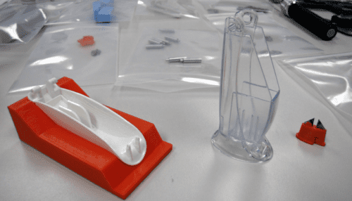 AmpliVue assay cartridge prototype on a red stand with surrounding clear molded components and small test parts on a lab bench.