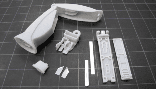 Prototype parts of the AmpliVue assay cartridge including housing pieces, internal inserts and small molded components laid out on a cutting mat.