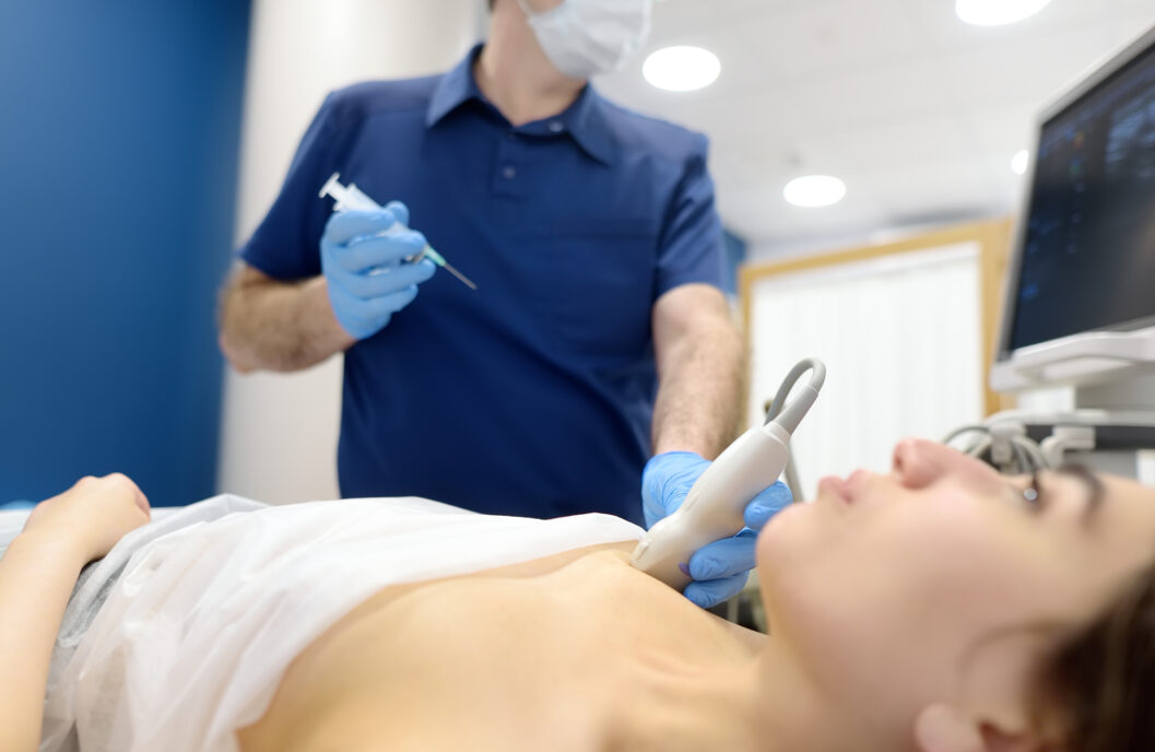 Mammalogist doctor examines a woman breasts and lymph nodes during appointment. Skillful oncologist puncture of mammary glands of young patient under review ultrasound for diagnosis of breast cancer.