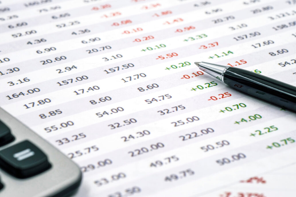 Spreadsheet displaying rows and columns of numerical data, some highlighted in green or red to indicate positive and negative values, with a pen and calculator placed nearby.