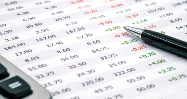 Spreadsheet displaying rows and columns of numerical data, some highlighted in green or red to indicate positive and negative values, with a pen and calculator placed nearby.