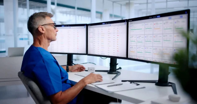 Connected care in practice as a clinician reviews patient monitoring data across three screens at a central workstation