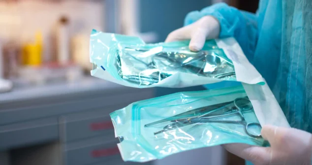 Gloved technician handling sterile packaged medical instruments prepared for radiation sterilization validation.