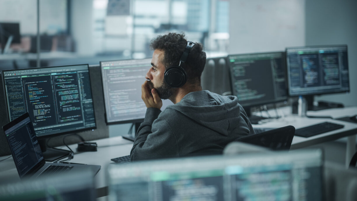 Office: Professional White IT Programmer Uses Headphones while Working on Desktop Computer. Male Website Developer, Software Engineer Developing App, Video Game. Listening to Podcast, Music.