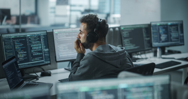 Office: Professional White IT Programmer Uses Headphones while Working on Desktop Computer. Male Website Developer, Software Engineer Developing App, Video Game. Listening to Podcast, Music.