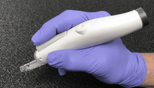 Gloved clinician holding the IOL injector handpiece, showing ergonomic grip and ready position for lens delivery.