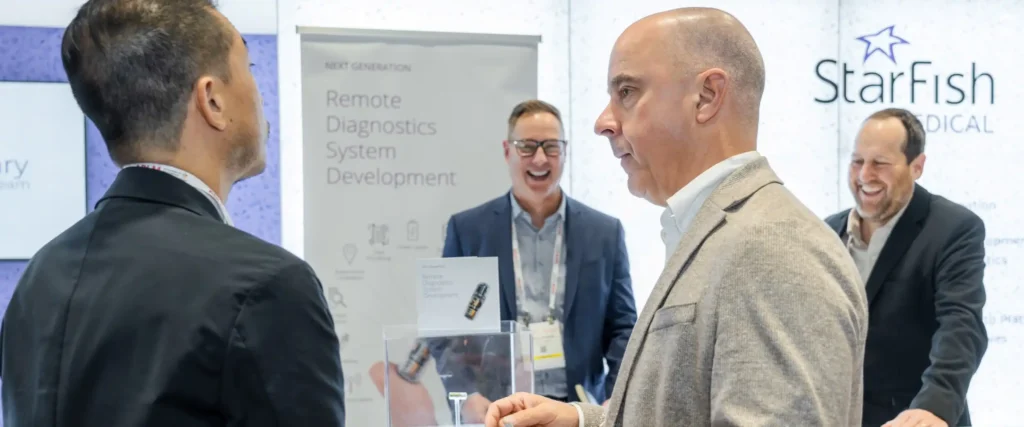 People networking at the StarFish Medical booth at the MedTech Conference 2024 with a display on remote diagnostics system development.