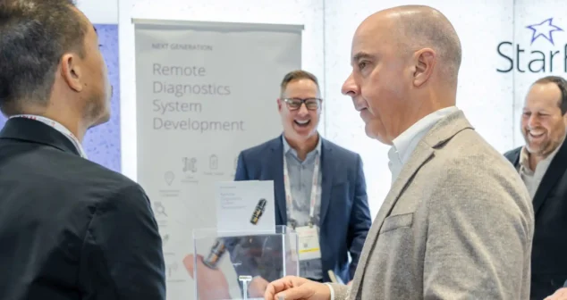 People networking at the StarFish Medical booth at the MedTech Conference 2024 with a display on remote diagnostics system development.