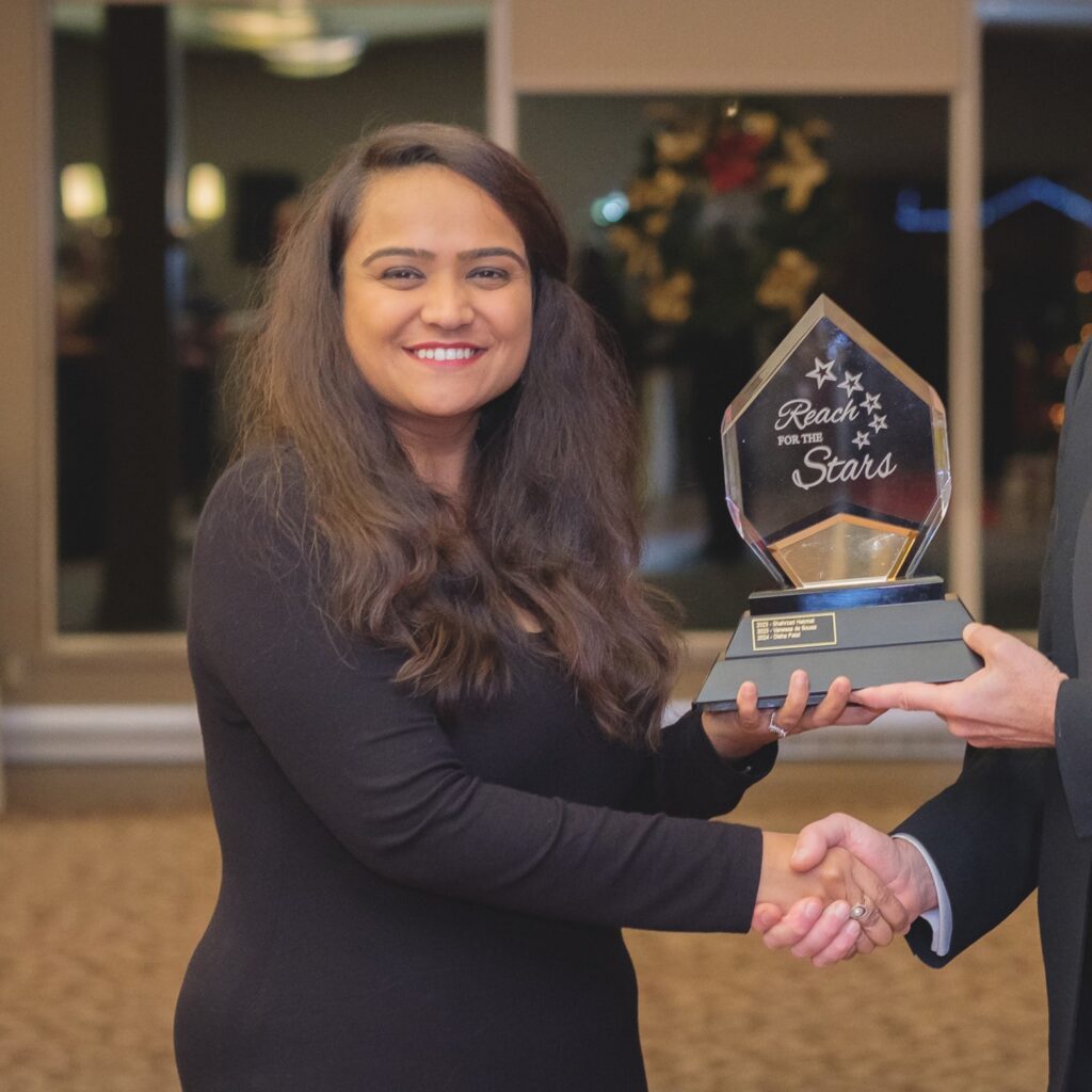 A woman with long hair wearing a black outfit holding an award that says "Reach for the Stars" while smiling.