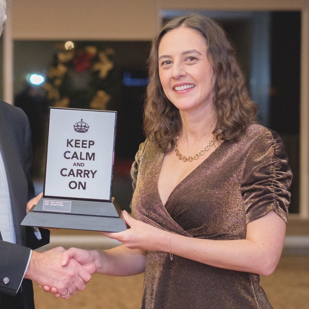 A woman dressed elegantly in a shimmering dress holding an award with "Keep Calm and Carry On" inscribed on it.