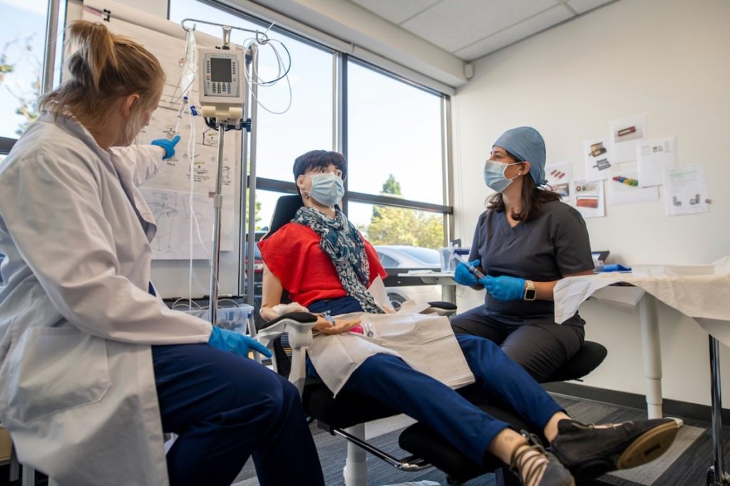 A doctor and a nurse sitting next to a dummy demonstrating the use of a medical device.