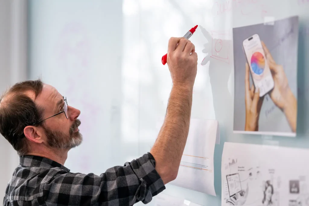 Product designer sketching early-phase concept wireframes on glass whiteboard during ideation session