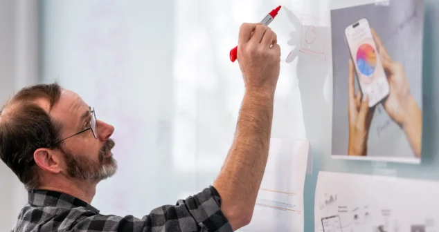 Product designer sketching early-phase concept wireframes on glass whiteboard during ideation session
