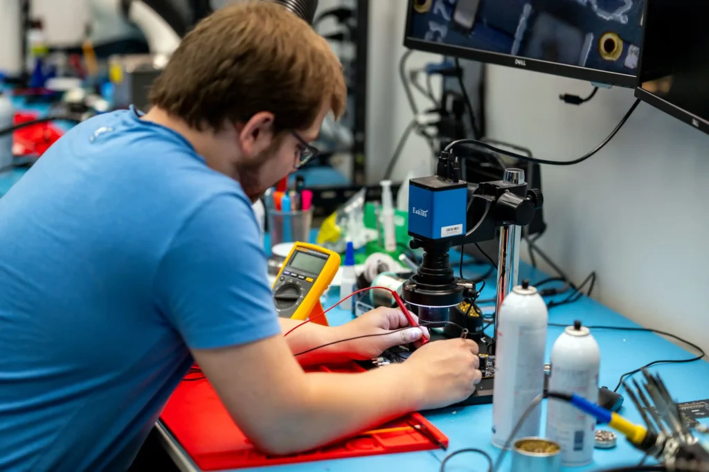 Engineer testing circuit board for portable medical device design using oscilloscope and microscope in electronics lab.