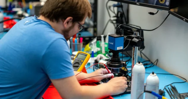 Engineer testing circuit board for portable medical device design using oscilloscope and microscope in electronics lab.