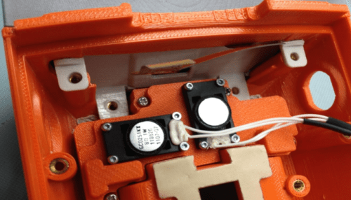 Close-up of an orange LVAD controller prototype showing internal wiring, fasteners, and mounted electronics.