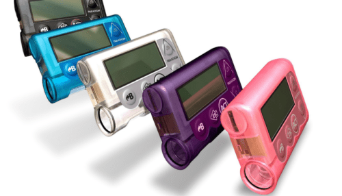 Multiple MiniMed insulin pumps in various colors arranged together, showing the compact screen, buttons and clip-on design.