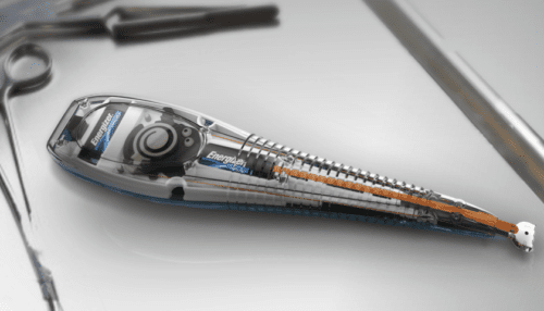 Ocular scleratome tool with transparent housing placed beside surgical instruments, showing internal structure and blade alignment.
