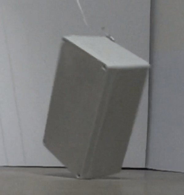 A high-speed video of a real rectangular enclosure being dropped diagonally onto a hard surface. The enclosure impacts one of its corners first and visibly bounces and tips after contact. The test mimics real-world physical conditions to evaluate mechanical robustness.