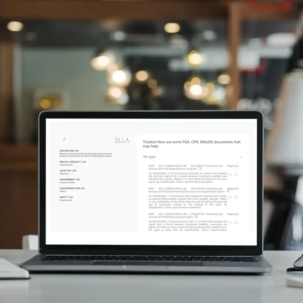 A laptop displaying a regulatory tool interface called "ELLA," showing FDA, CFR, and MAUDE documentation with editable categories such as medical specialty, objective, and safety. The workspace is a modern office with blurred decor in the background.