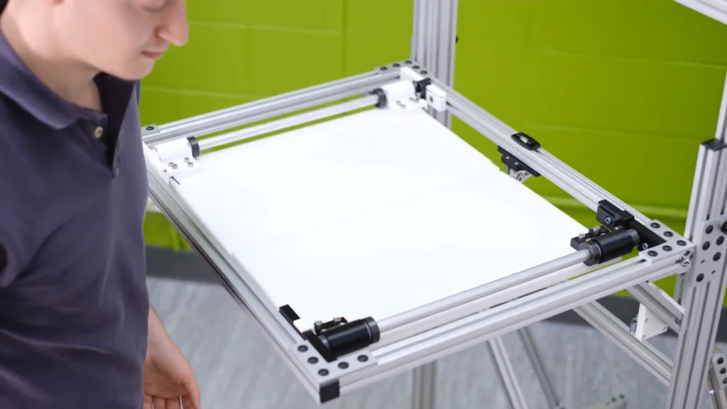 Technician operating a custom aluminum-framed drop test rig with a white platform and green background wall.