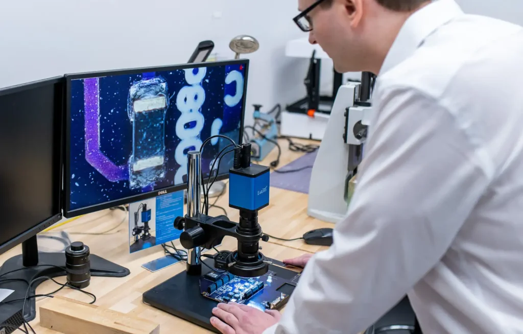 Biomedical engineer inspecting a medical device prototype under a digital microscope in a laboratory setting.