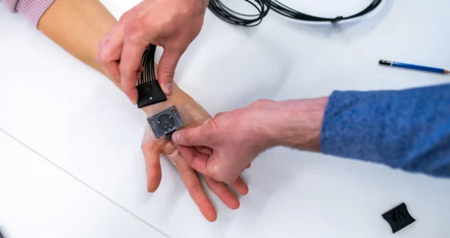 Hands applying a wearable medical sensor prototype to a patient’s wrist during testing.