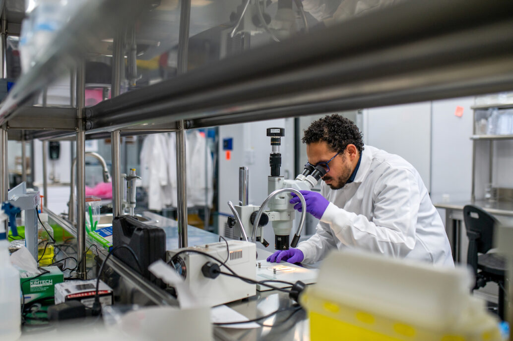 Scientist with goggles working in lab seen through shelving.