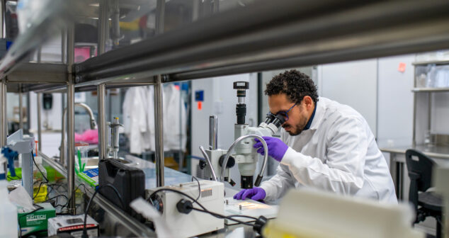 Qualifying a Development Partner Scientist with goggles working in lab seen through shelving.