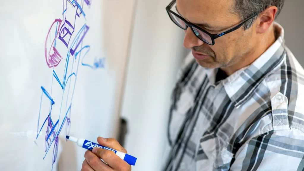 Engineer sketching early medical device concepts on a whiteboard during initial design exploration.