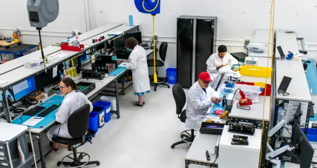 Technicians in lab coats assembling and testing medical devices at workstations inside a clean, organized MedTech manufacturing facility.