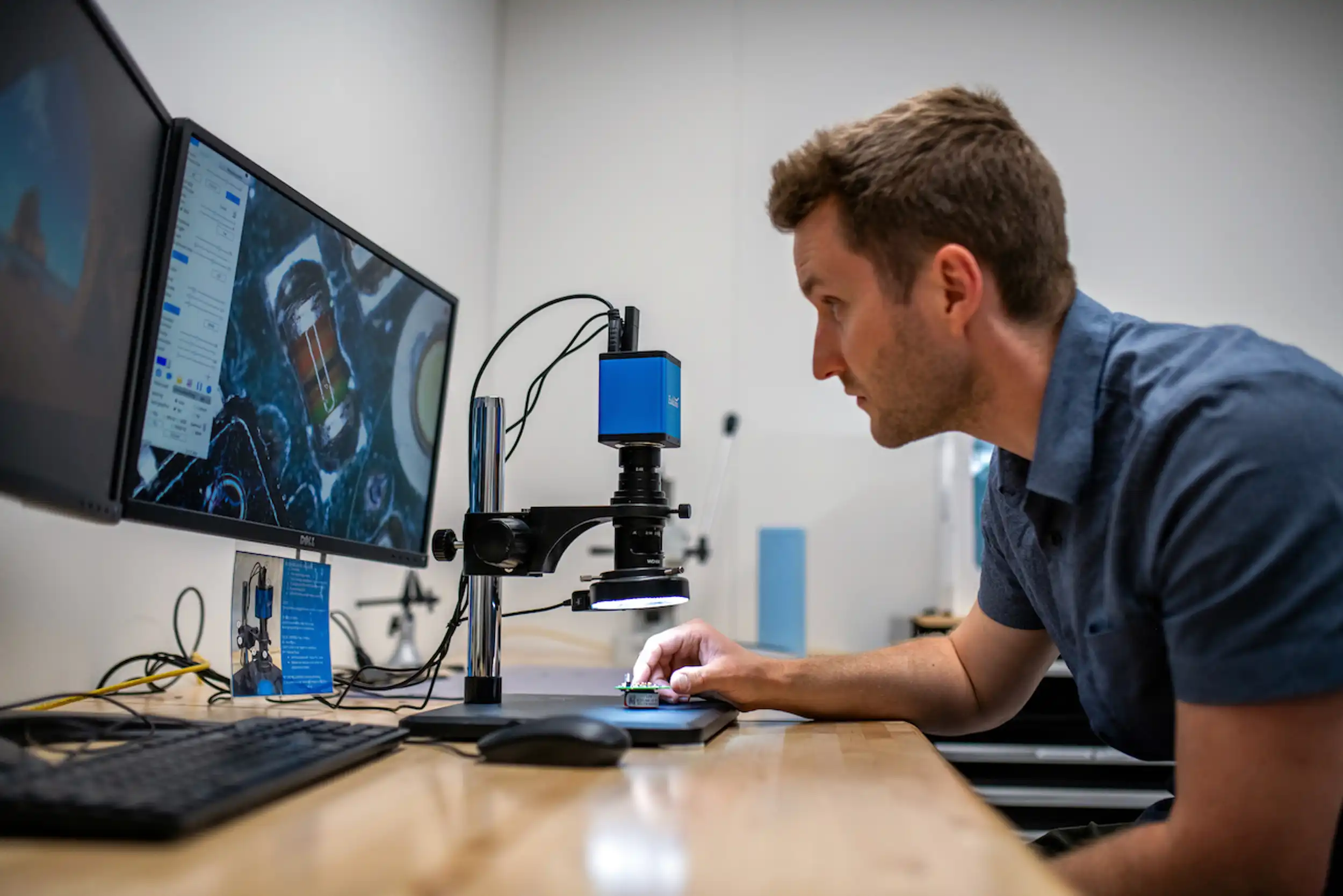 Engineer using a digital microscope and computer monitor to analyze medical device components.