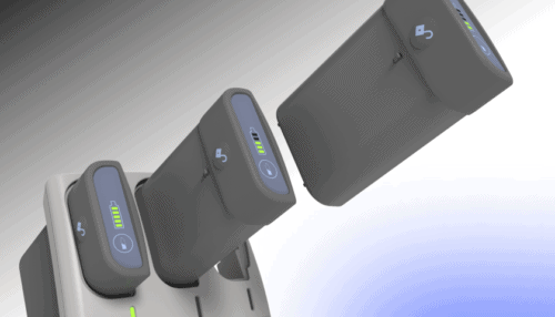 Rendered LVAD battery packs being inserted into a multi-slot charging dock with illuminated charge indicators.