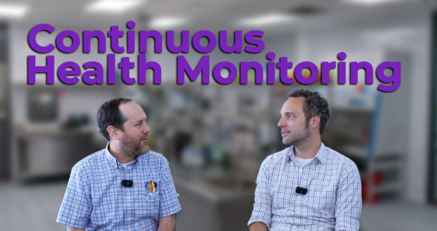 Two professionals in a laboratory setting discuss health monitoring innovations. The text overlay reads "Continuous Health Monitoring," emphasizing advancements in wearable devices and real-time data tracking for improved healthcare outcomes.