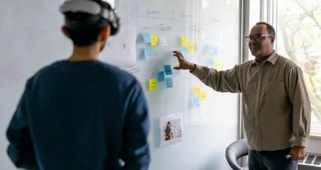 Two medtech professionals collaborating at a whiteboard covered in UX design notes and post-its, discussing user experience strategy for a medical device.