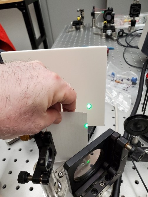 a hand holding an index card with a green laser on the edge of the card.