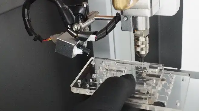 Automated dispensing needle applying adhesive to a transparent microfluidic cartridge during assembly
