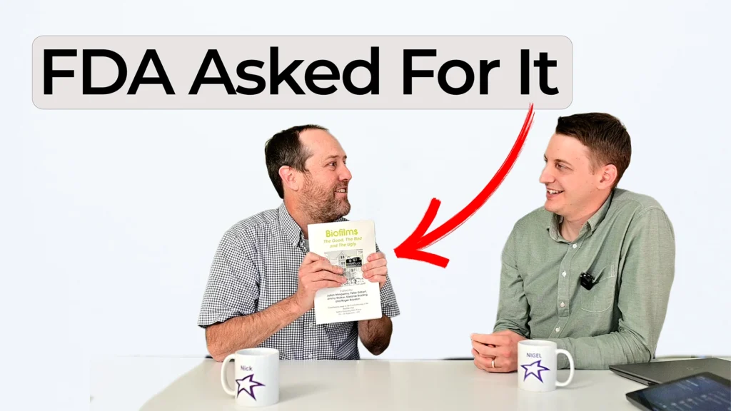 Nick showing a biofilm conference book while Nigel listens, with overlay text reading FDA Asked For It and a red arrow pointing to the book.