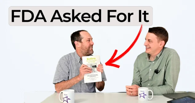 Nick showing a biofilm conference book while Nigel listens, with overlay text reading FDA Asked For It and a red arrow pointing to the book.