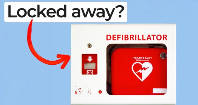 A red defibrillator inside a white wall-mounted cabinet labeled DEFIBRILLATOR. A red arrow points to it, with overlay text reading ‘Locked away?’ in bold black letters on a white highlight.