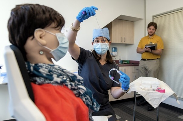 Man observing clinician using medical equipment on a dummy doll