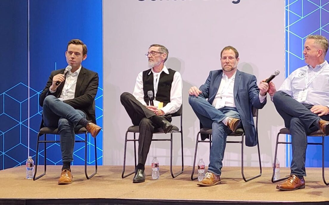 Panel discussion at the Silicon Valley MEDdevice event, with four seated panelists and one standing moderator on the Center Stage. The backdrop features geometric patterns and event branding, with a palm plant visible on the side of the stage.